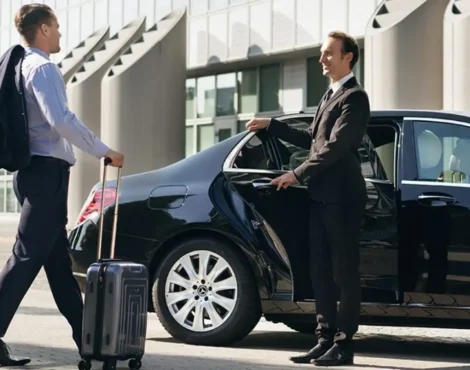 Chauffeur opening door of luxury black car for business traveler with suitcase, showcasing professional airport pickup or intercity transfer service.