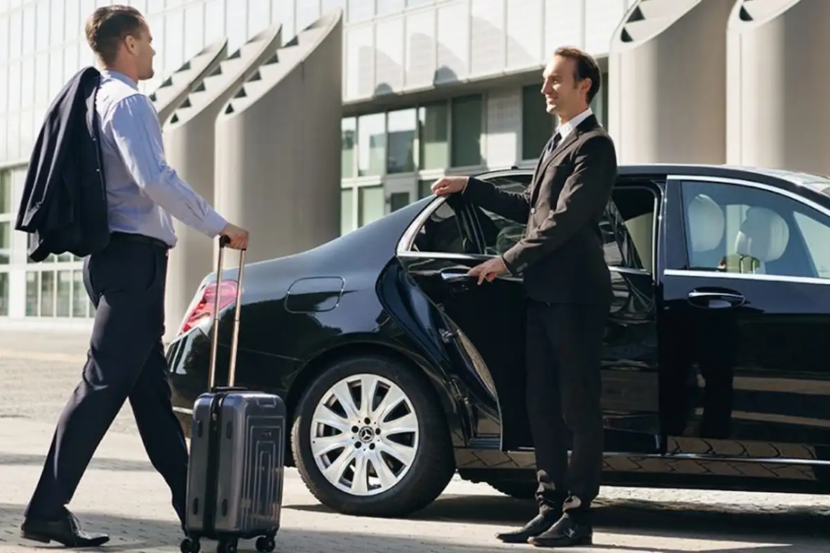 Chauffeur opening door of luxury black car for business traveler with suitcase, showcasing professional airport pickup or intercity transfer service.