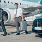 Business travelers in suits wearing masks walking from airplane toward luxury chauffeur car, highlighting safe and professional airport transfer service.