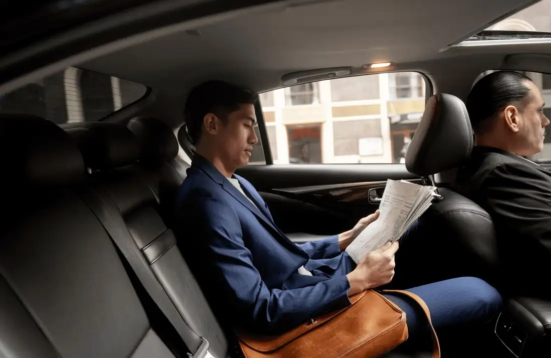 Corporate businessman reading newspaper in the backseat of a luxury chauffeur-driven car, enjoying a comfortable and productive executive ride.