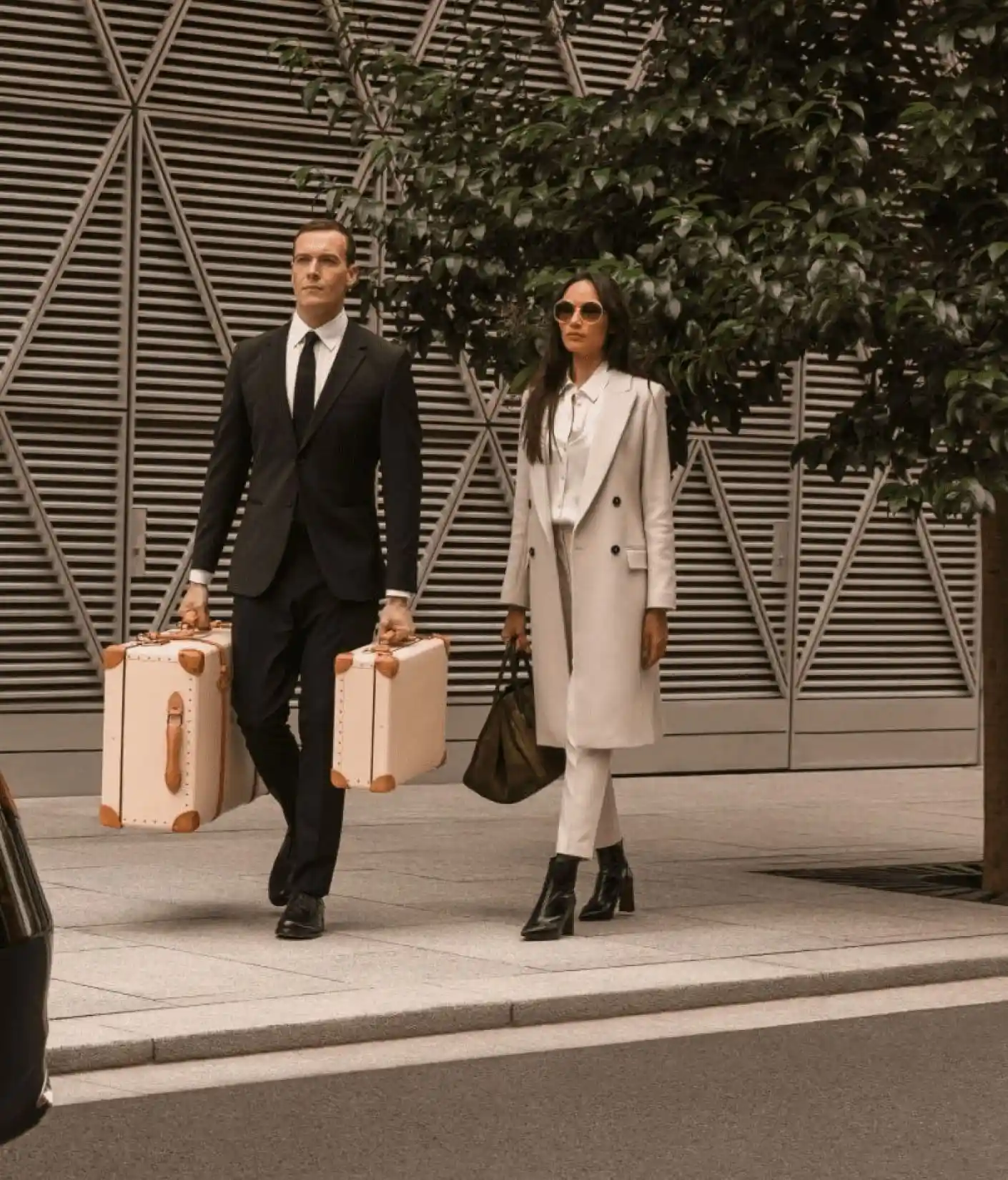 Stylish couple in formal attire arriving with luxury suitcases for chauffeur pickup, showcasing premium airport transfer or executive travel service.